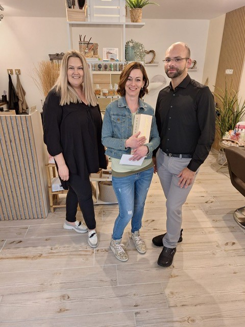Drei Personen strahlen bei der feierlichen Firmeneröffnung von Windberger in Baden – Inhaberin mit Präsentkorb im modern gestalteten Ladenlokal.