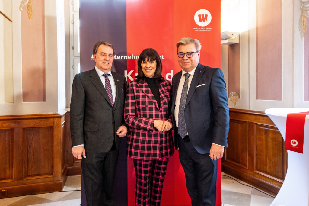 Auf dem Bild Wolfang Ecker in dunklem Anzug, Martha Schulz in der Mitte mit Muster Blazer und Hose sowie Harald Servus links vor einem Roll Up des Wirtschaftsbundes Niederösterreich