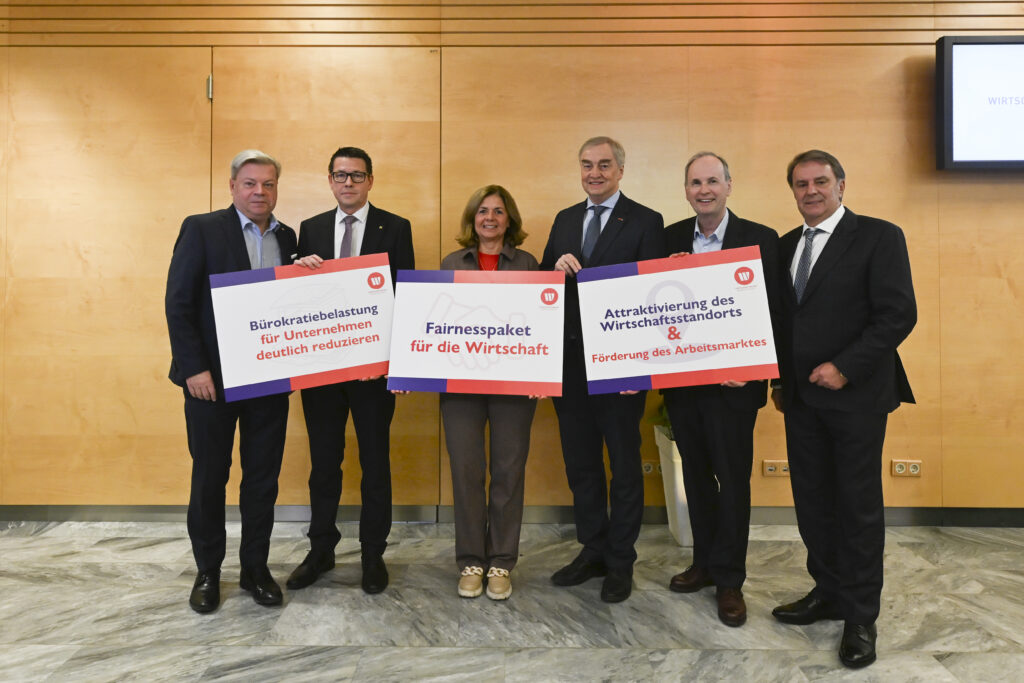 Vor einer Holzwand befinden sich Teile des Präsidiums der WKNÖ sowie Harald Servus. Sie halten Taferl mit Forderungen in die Kamera