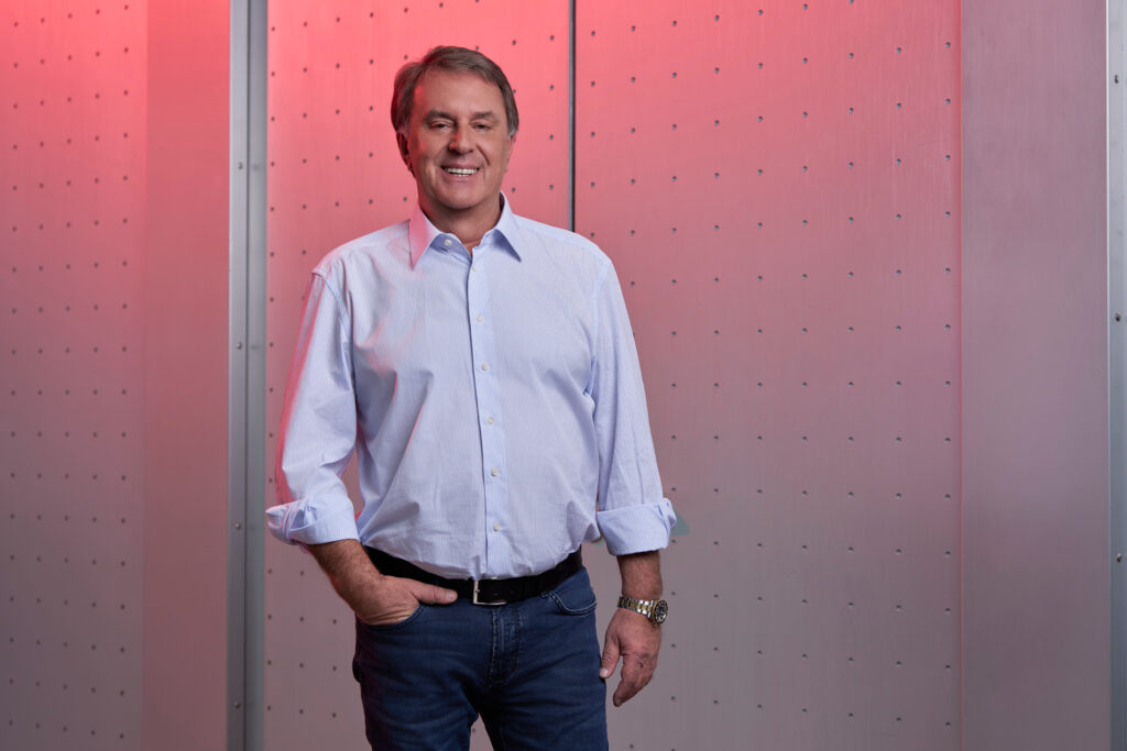 Wolfgang Ecker, Hemd, Hand in der Tasche, vor einem rot beleuchteten Hintergrund.