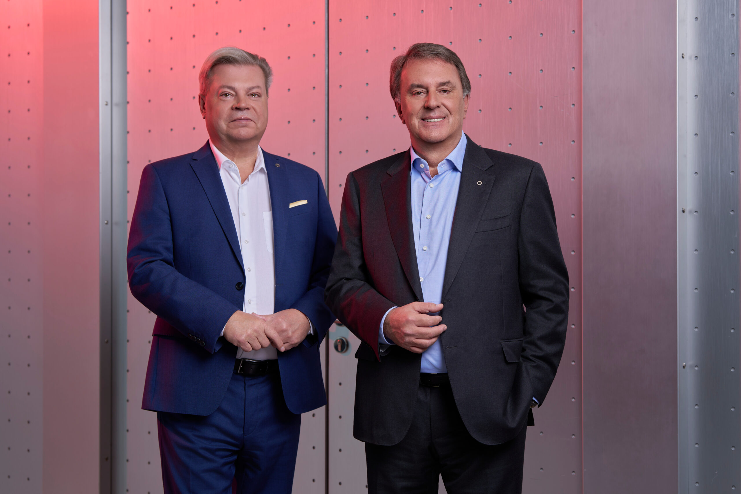 Harald Servus links im dunklen Anzug und Wolfgang Ecker im dunklen Anzug vor rotem Hintergrund